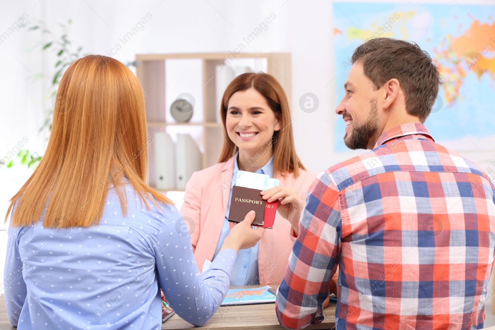 Photo of Female manager giving passports with tickets to couple in travel agency