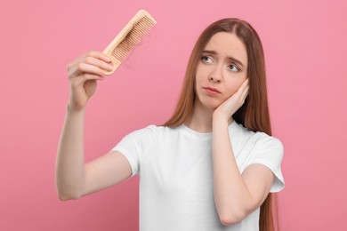 Photo of Upset woman holding comb with lost hair on pink background. Alopecia problem