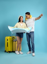 Couple of tourists with map and suitcases on light blue background