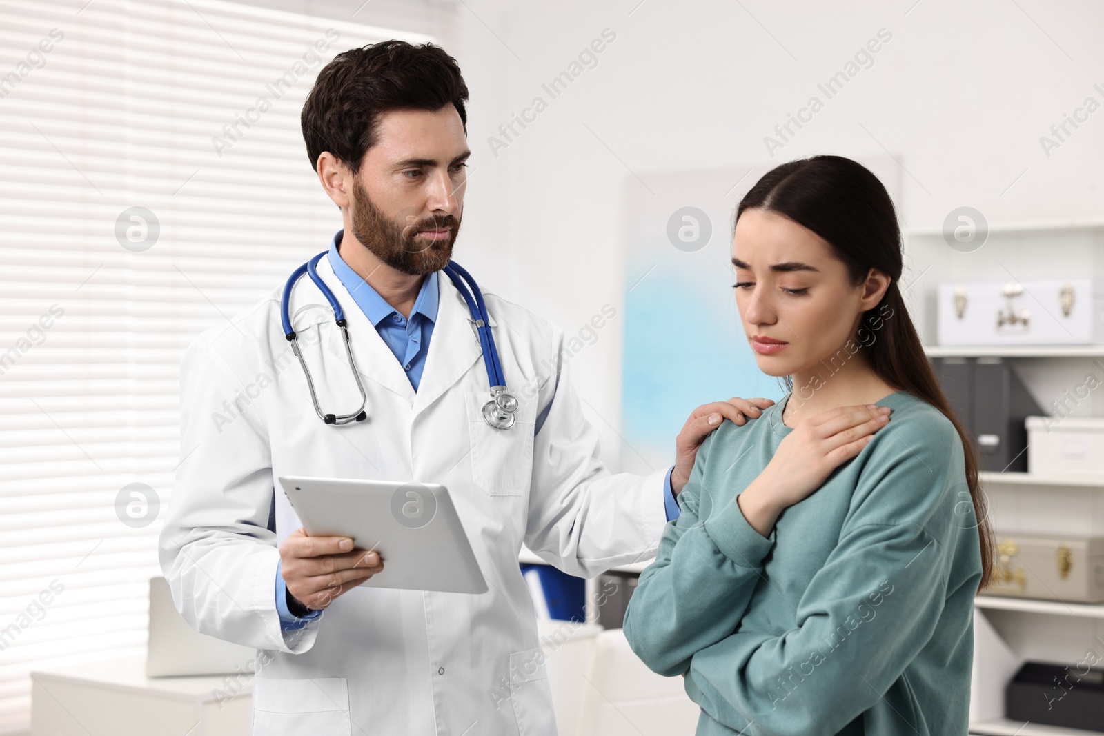 Photo of Doctor with tablet consulting patient during appointment in clinic