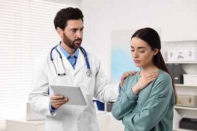 Doctor with tablet consulting patient during appointment in clinic