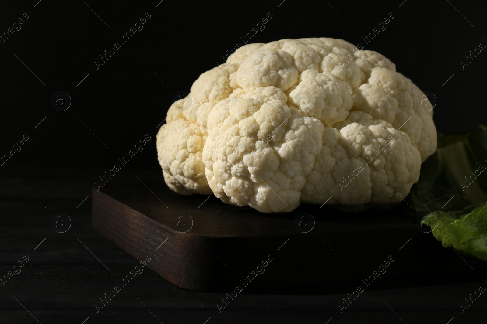 Photo of Fresh raw cauliflower on black wooden table, closeup
