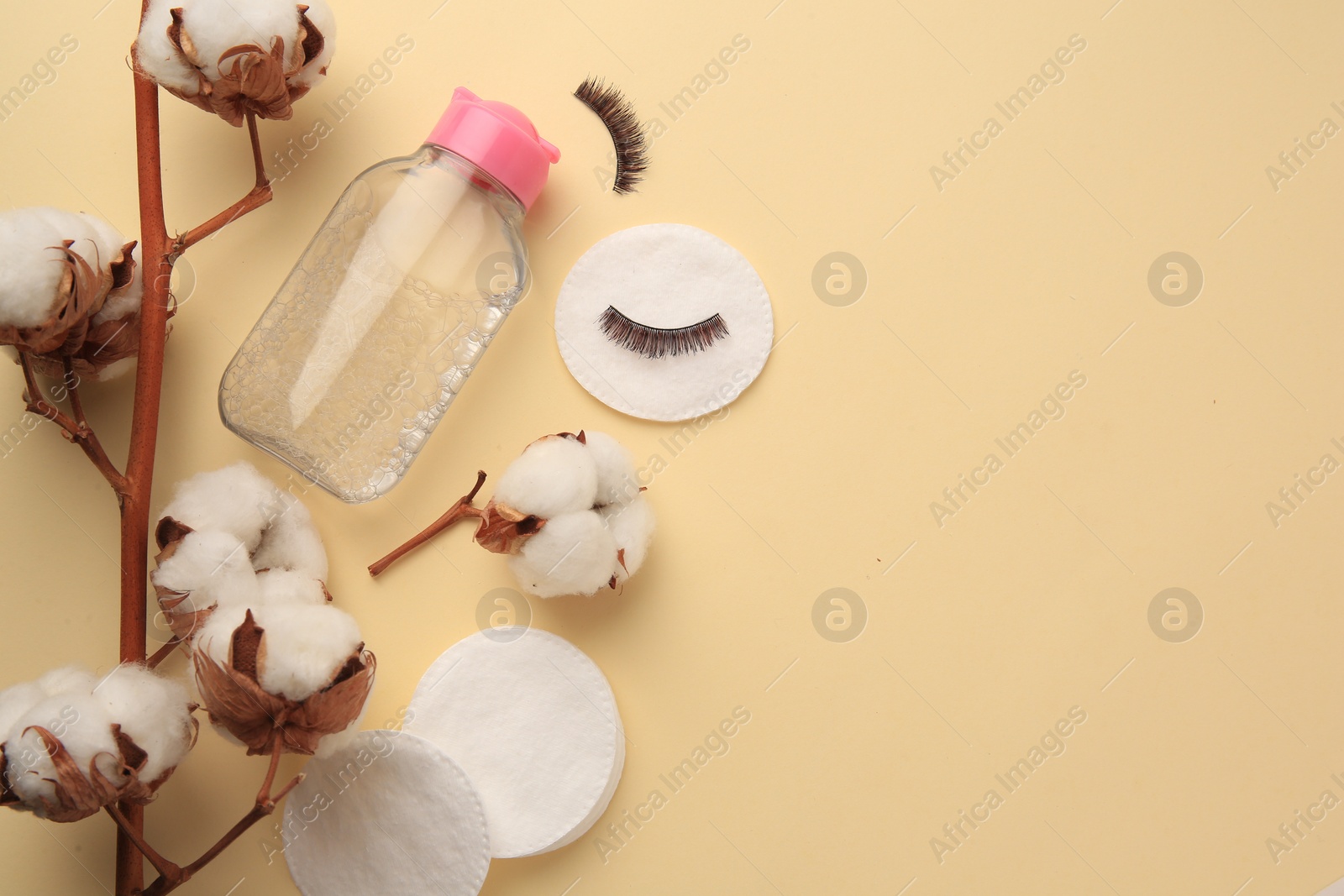 Photo of Bottle of makeup remover, cotton flowers, pads and false eyelashes on yellow background, flat lay. Space for text