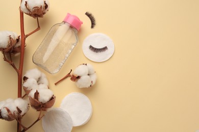 Bottle of makeup remover, cotton flowers, pads and false eyelashes on yellow background, flat lay. Space for text