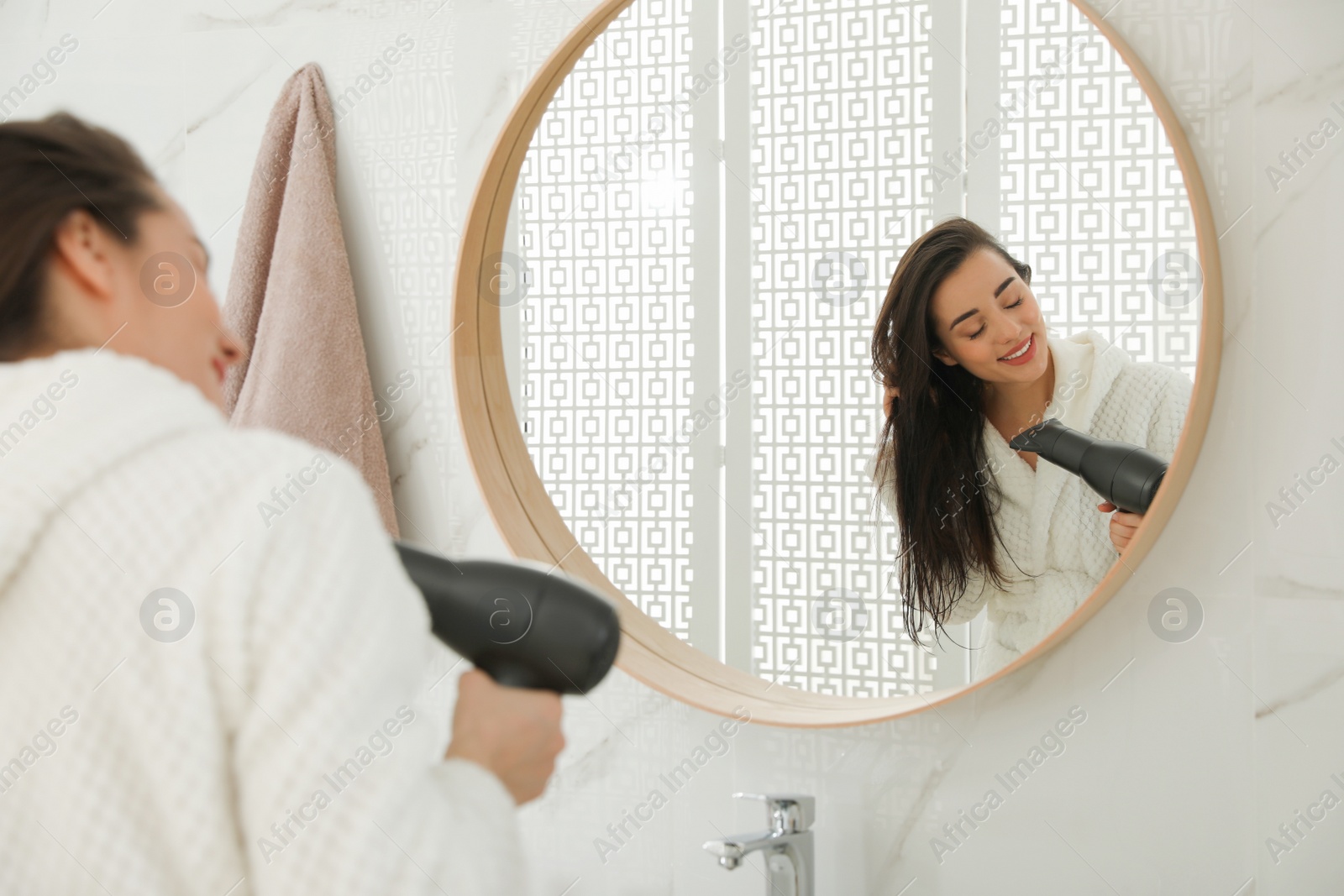 Photo of Beautiful young woman using hairdryer in bathroom