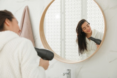 Photo of Beautiful young woman using hairdryer in bathroom