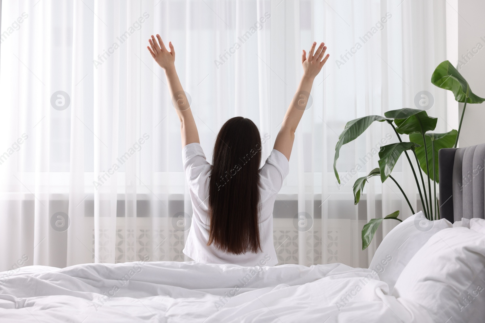 Photo of Woman stretching on bed at home, back view. Lazy morning