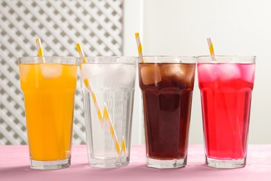 Photo of Glasses of different refreshing soda water with ice cubes and straws on pink wooden table