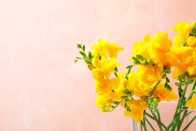 Photo of Beautiful blooming yellow freesias in glass vase against pink background. Space for text