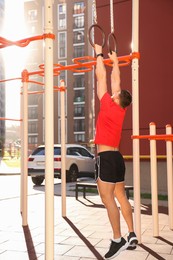Photo of Man training on gymnastic rings at outdoor gym on sunny day