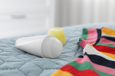 Photo of Female roll-on deodorant and striped t-shirt on bed, closeup