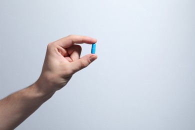 Photo of Man holding pill on light grey background, closeup. Space for text