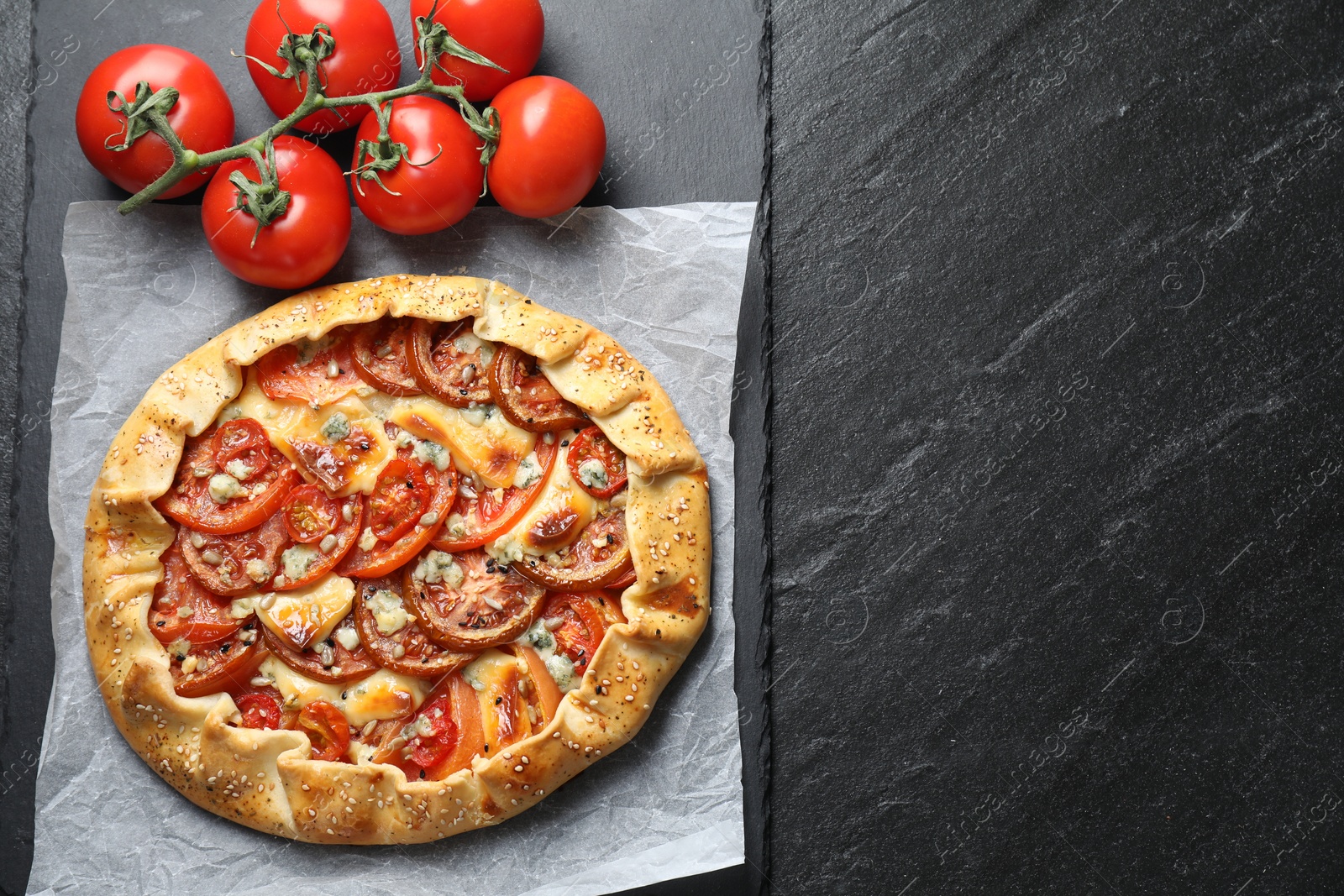 Photo of Tasty galette with tomato and cheese (Caprese galette) on dark textured table, top view. Space for text