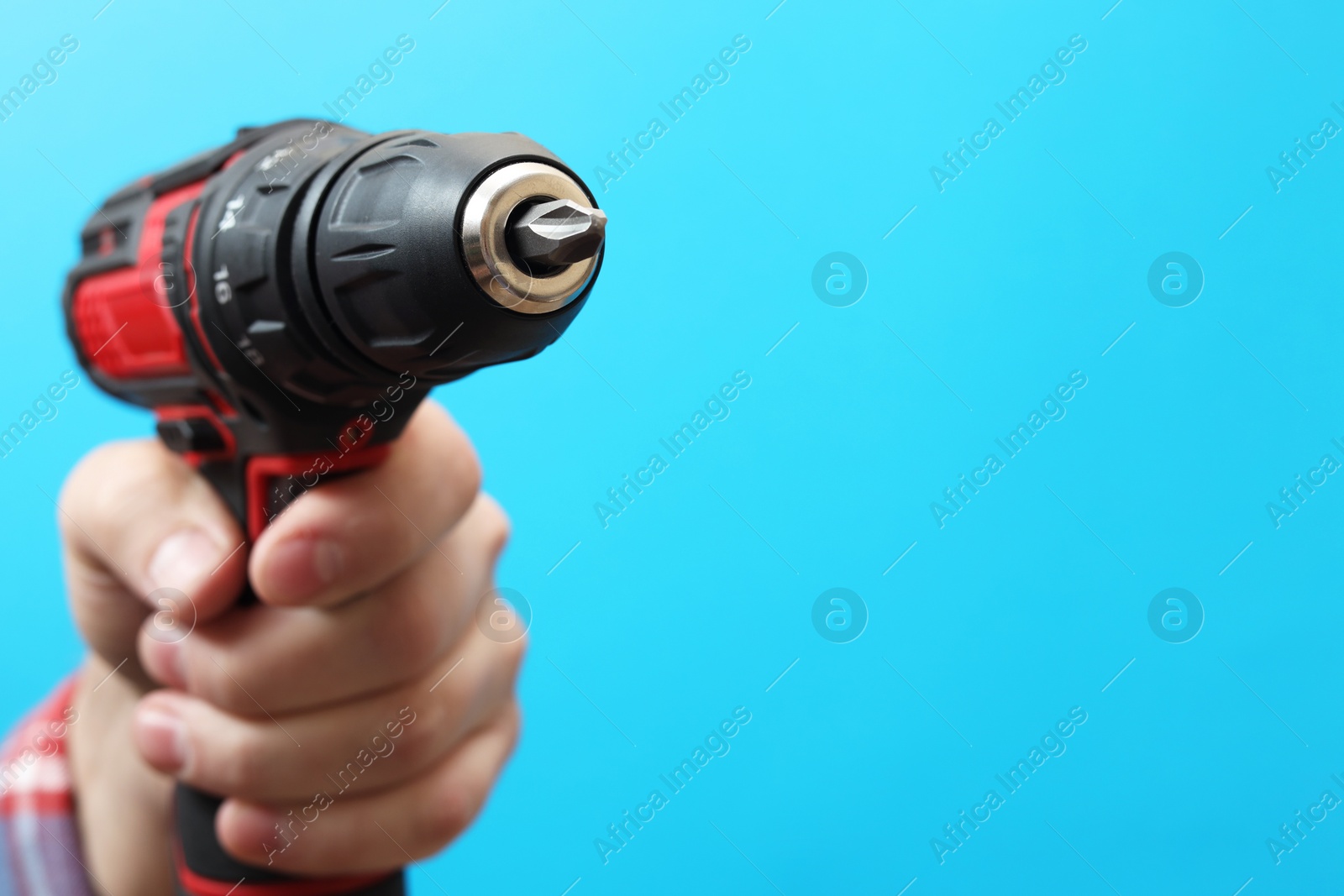 Photo of Handyman holding electric screwdriver on light blue background, closeup. Space for text