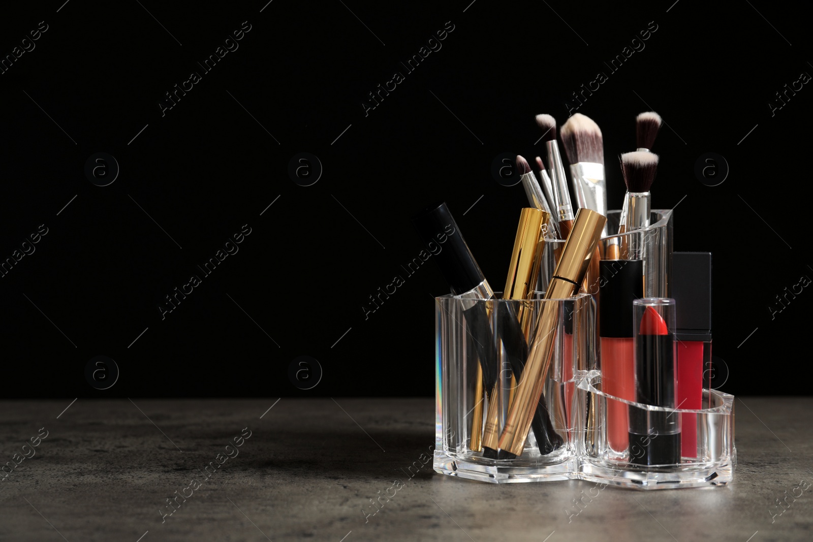 Photo of Lipstick holder with different makeup products on table against black background. Space for text