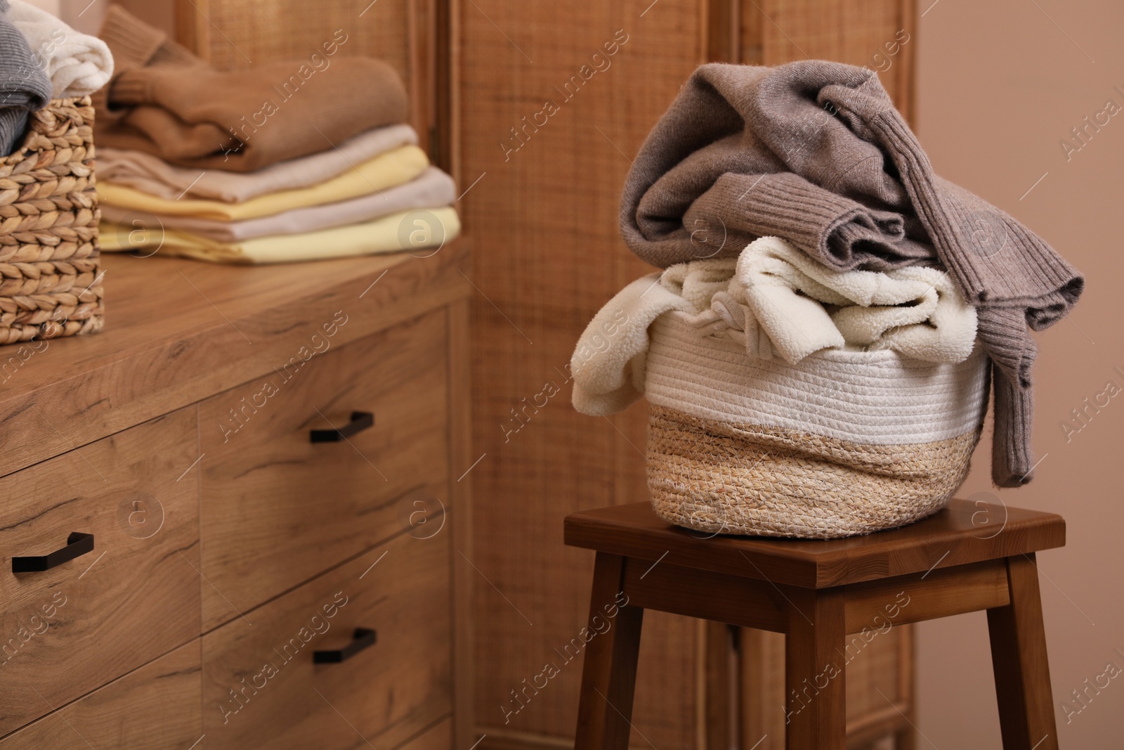 Photo of Wicker laundry basket overfilled with clothes on wooden stool indoors