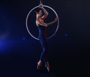 Photo of Young woman performing acrobatic element on aerial ring against dark background