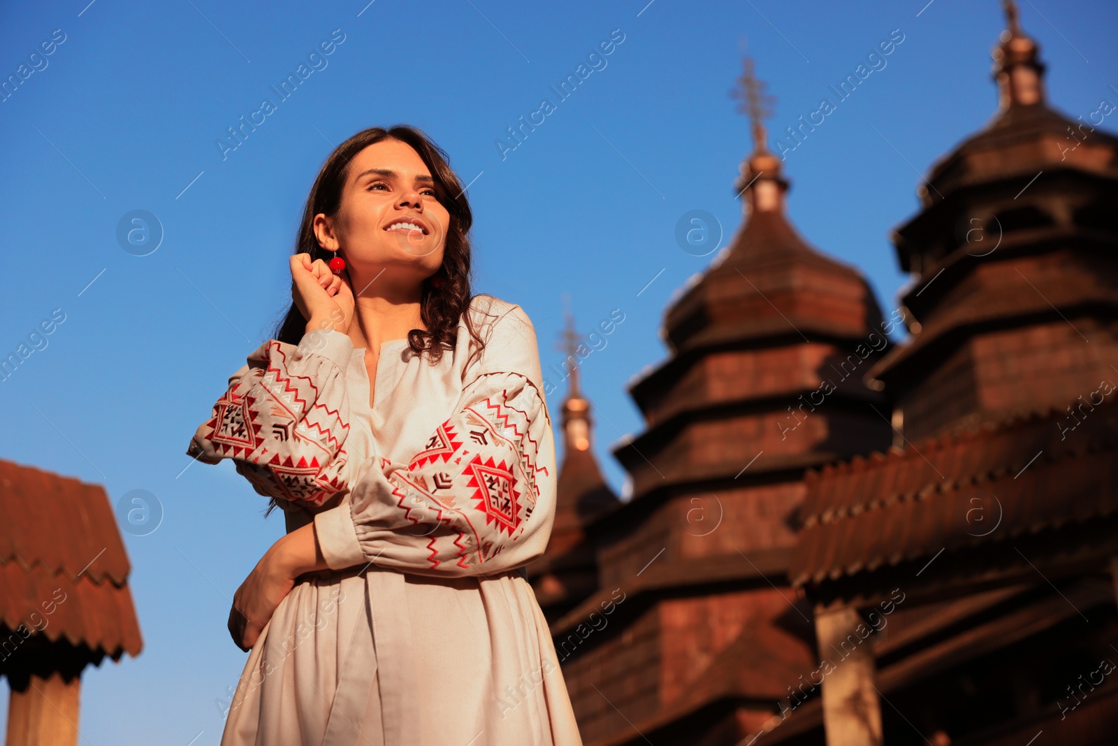 Photo of Beautiful woman wearing embroidered dress near old wooden church in village. Ukrainian national clothes