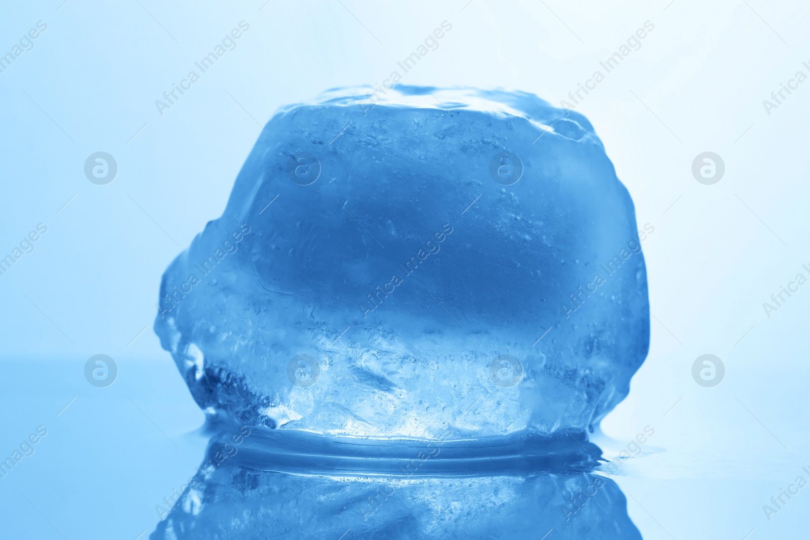 Photo of Crystal clear ice cube on light blue background, closeup. Color tone effect