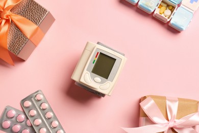 Blood pressure monitor, pills and boxes on pink background, flat lay. Medical gift