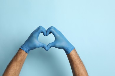 Photo of Doctor in medical gloves making heart with hands on light blue background, closeup. Space for text