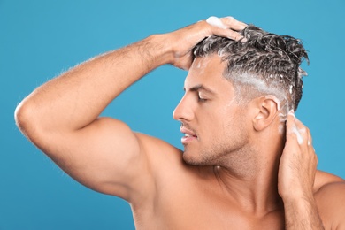 Photo of Handsome man washing hair on light blue background
