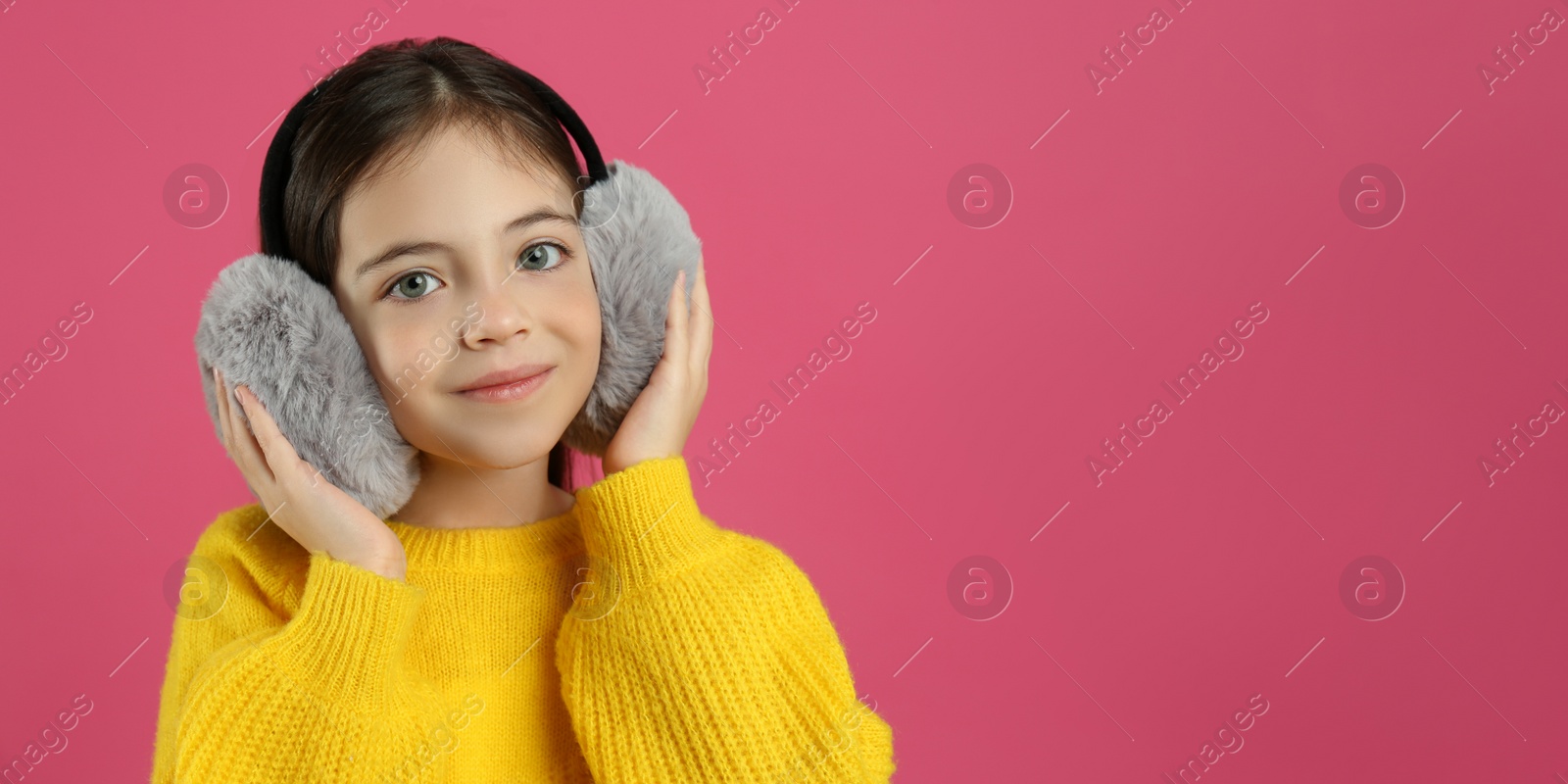 Photo of Cute little girl wearing stylish earmuffs on pink background