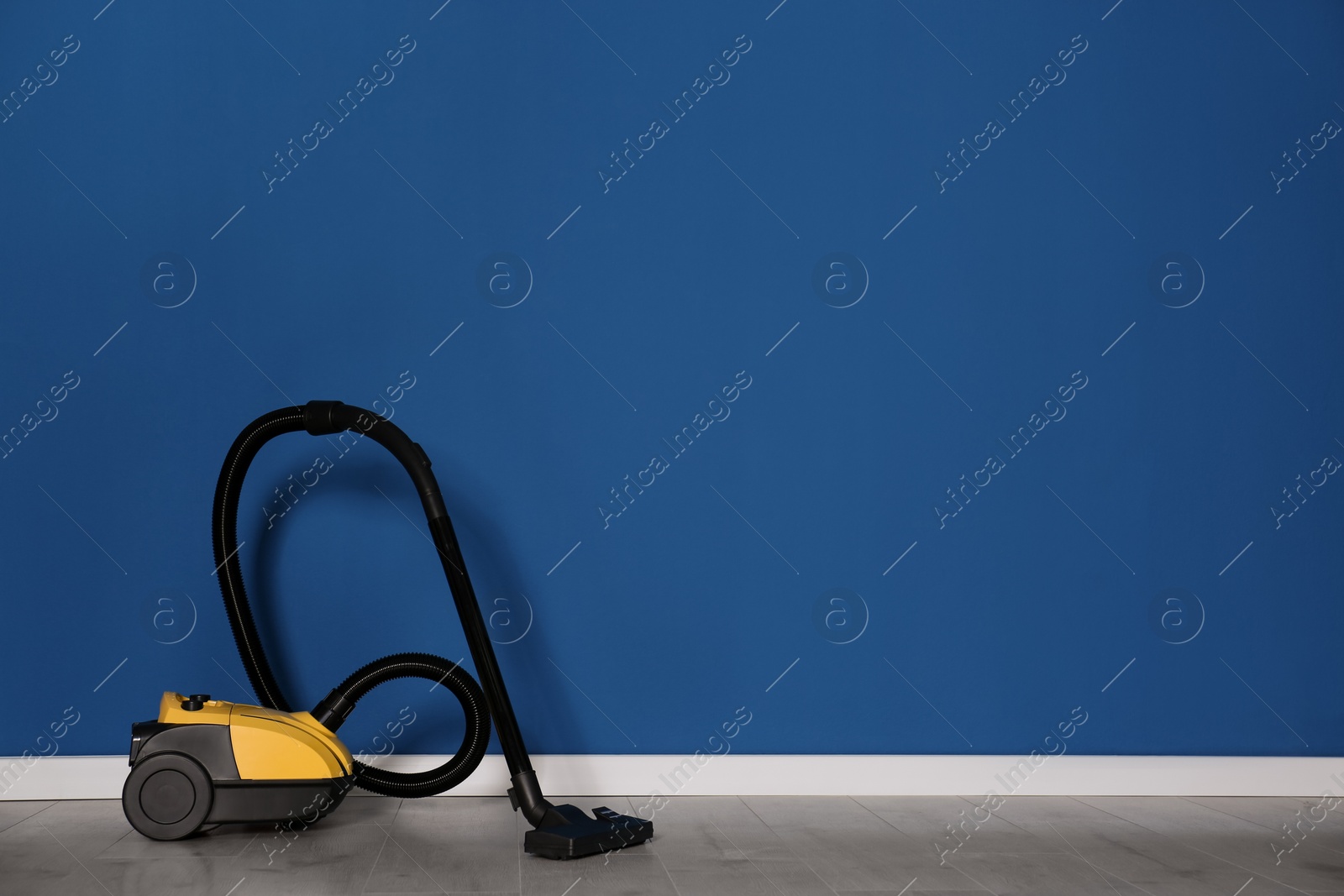 Photo of Modern yellow vacuum cleaner on floor near blue wall, space for text