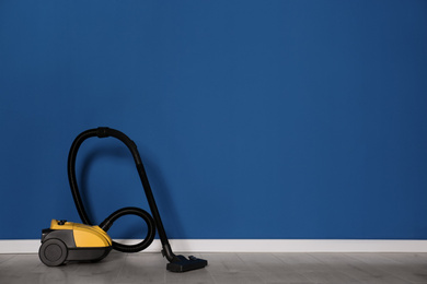 Modern yellow vacuum cleaner on floor near blue wall, space for text