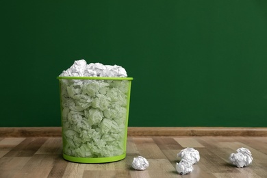 Photo of Metal bin with crumpled paper on floor against color wall, space for text