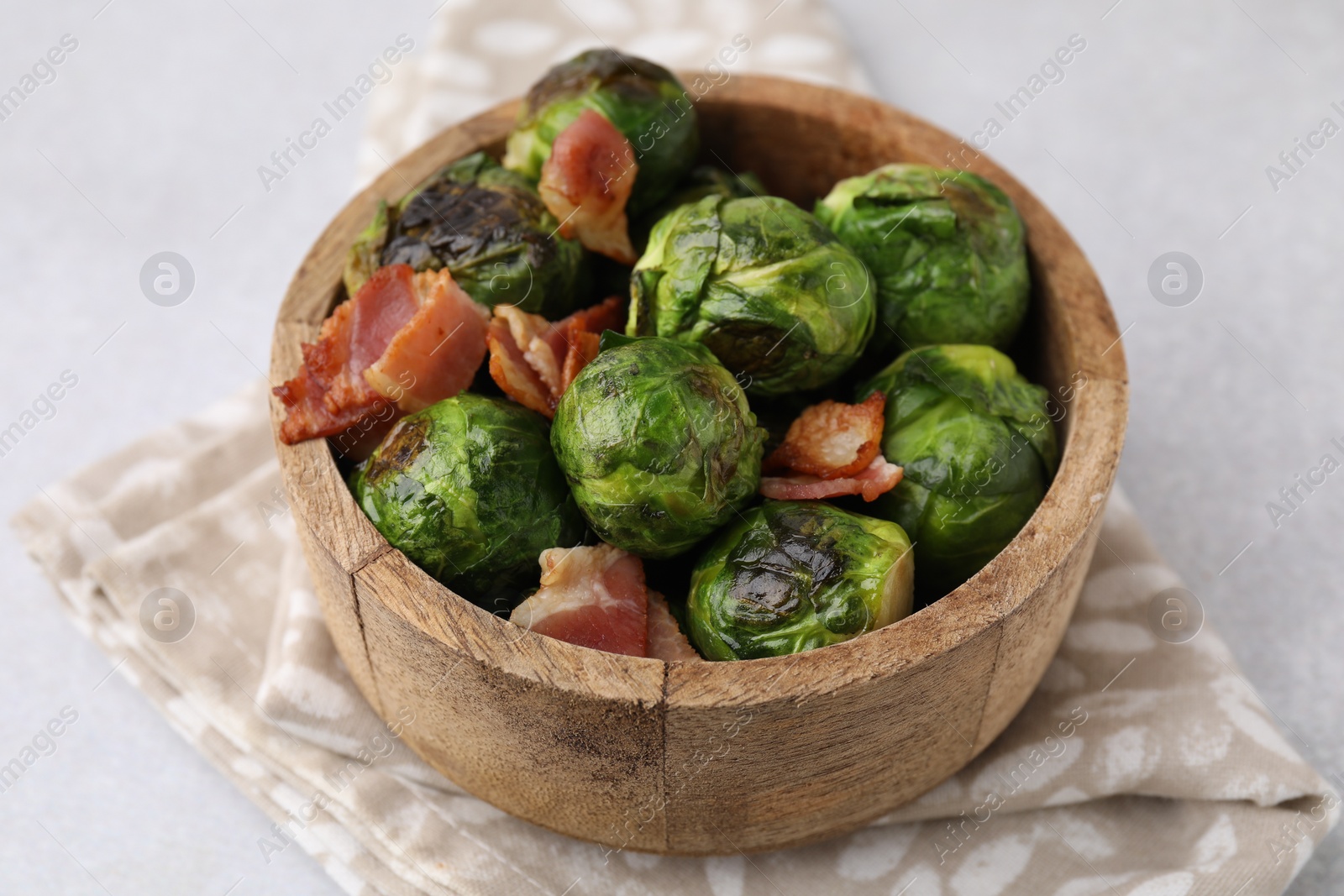 Photo of Delicious roasted Brussels sprouts and bacon in bowl on light table, closeup