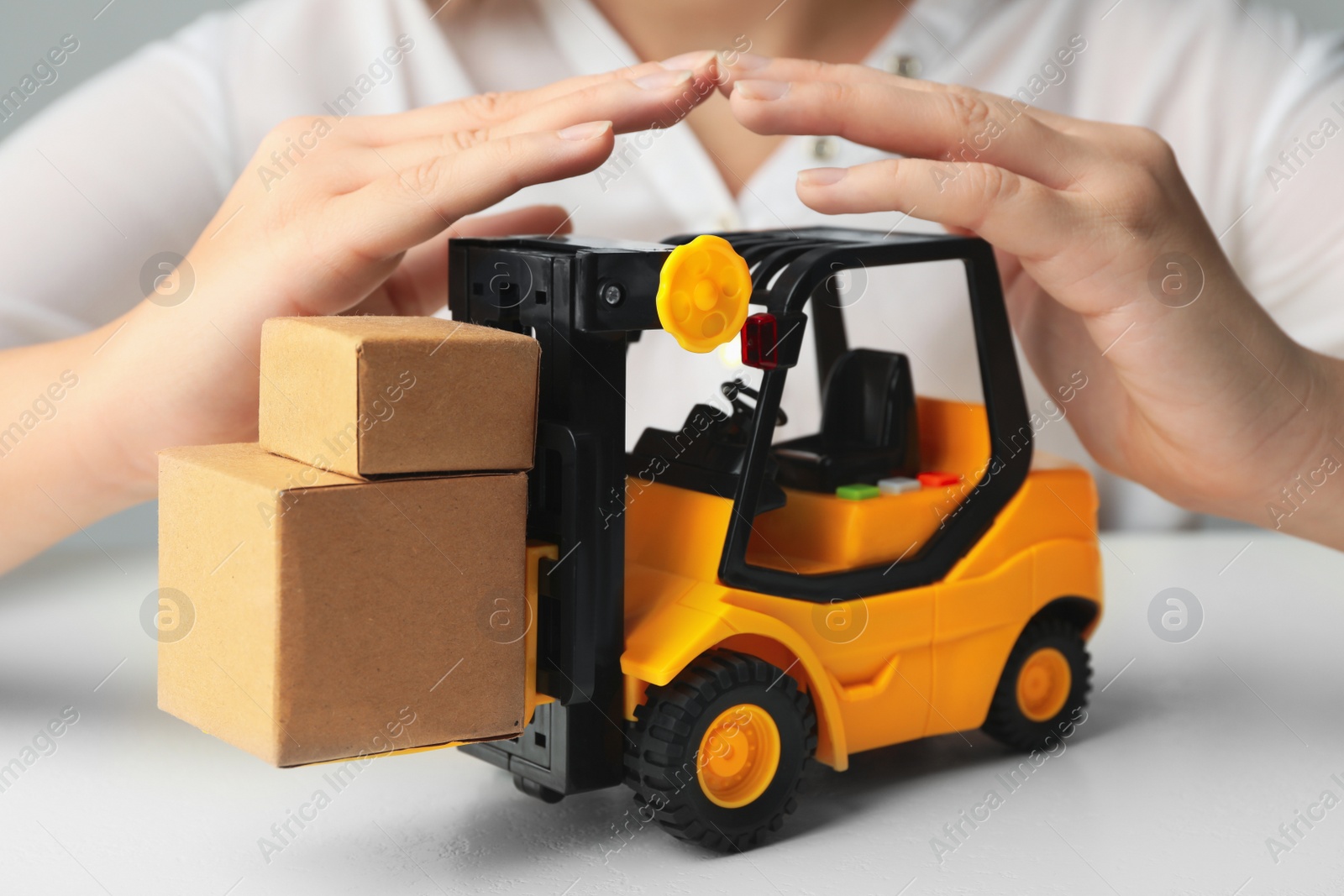 Photo of Woman covering toy forklift at white table, closeup. Logistics and wholesale concept