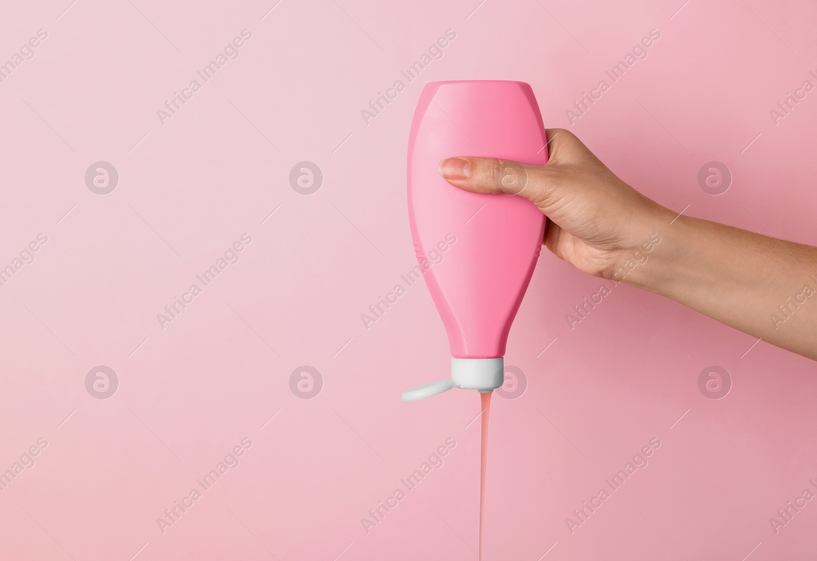 Photo of Woman pouring cosmetic product from bottle on color background, closeup. Space for text