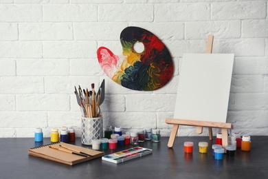 Easel with various artist tools on table against brick wall. Space for text
