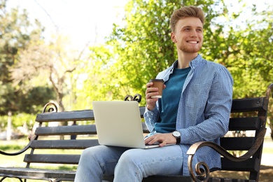 Image of Young man with paper cup of coffee working on laptop in park