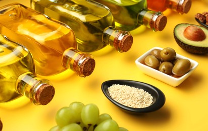 Vegetable fats. Different oils in glass bottles and ingredients on yellow table, closeup