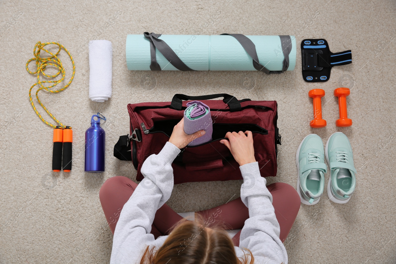 Photo of Woman packing sports stuff for training into bag on floor, top view