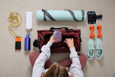 Photo of Woman packing sports stuff for training into bag on floor, top view