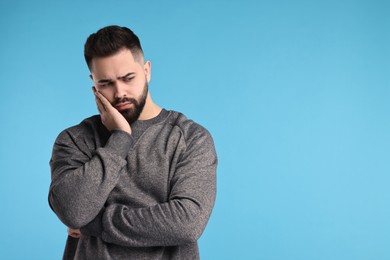 Portrait of sad man on light blue background, space for text