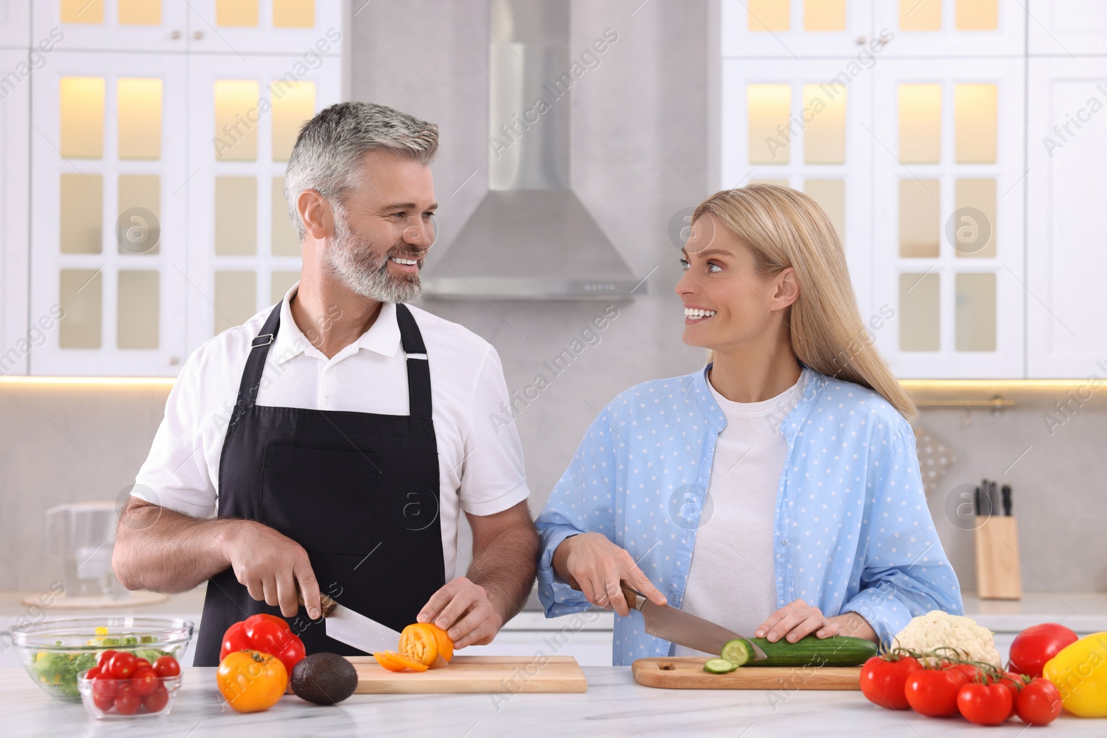 Photo of Happy affectionate couple cooking together at white table in kitchen