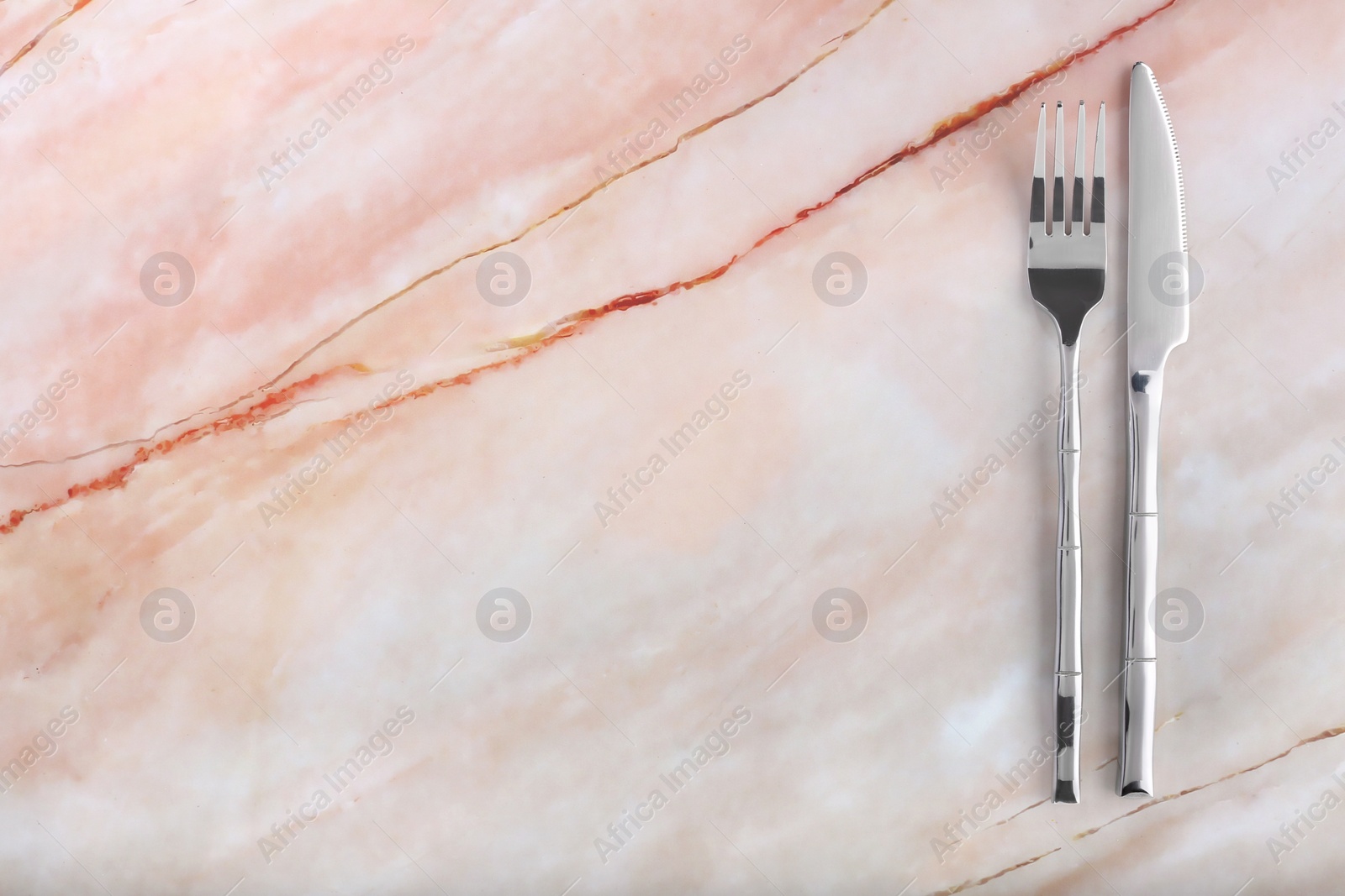 Photo of Shiny fork and knife on pink marble table, flat lay. Space for text