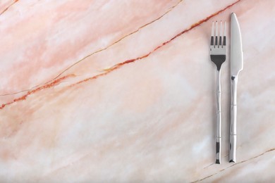 Shiny fork and knife on pink marble table, flat lay. Space for text