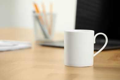 Photo of White ceramic mug on wooden table at workplace. Mockup for design