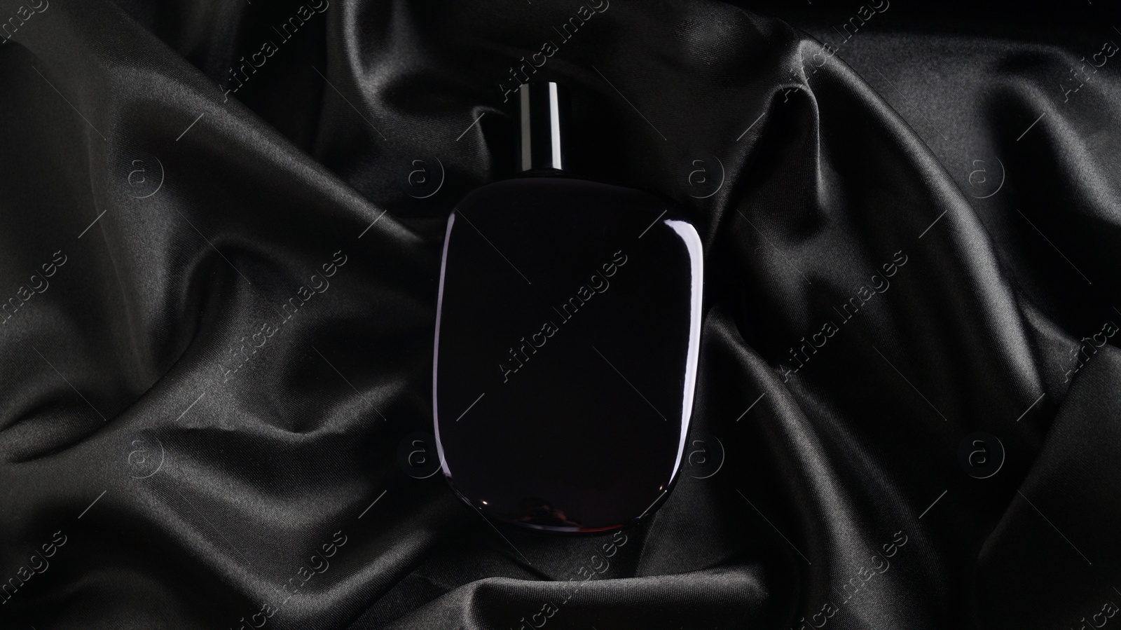 Photo of Luxury bottle of perfume on black silk, top view