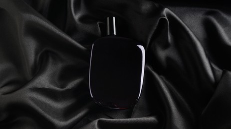Photo of Luxury bottle of perfume on black silk, top view