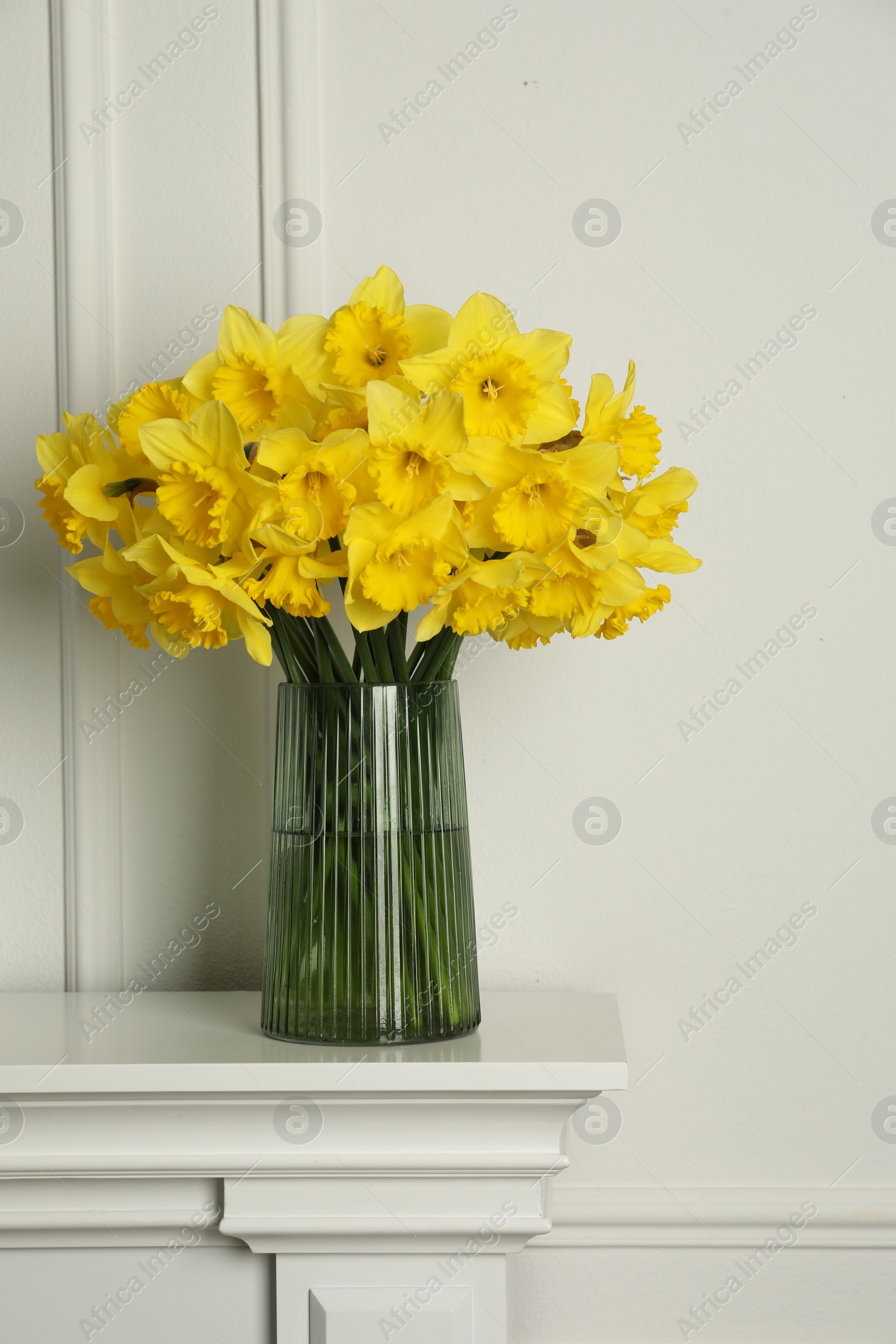 Photo of Beautiful daffodils in vase on table near white wall indoors