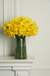 Photo of Beautiful daffodils in vase on table near white wall indoors