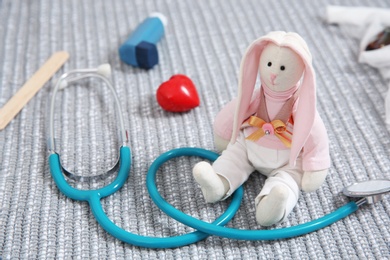 Photo of Composition with toy bunny, stethoscope and heart on fabric. Children's doctor