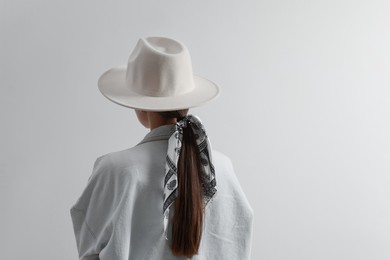 Young woman with hat and stylish bandana on light background, back view. Space for text