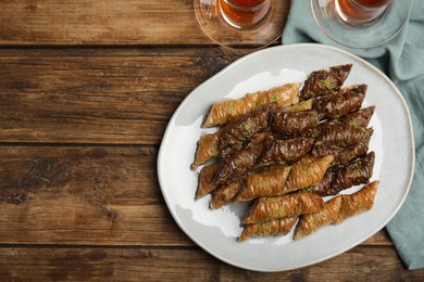 Delicious baklava with pistachios and hot tea on wooden table, flat lay. Space for text